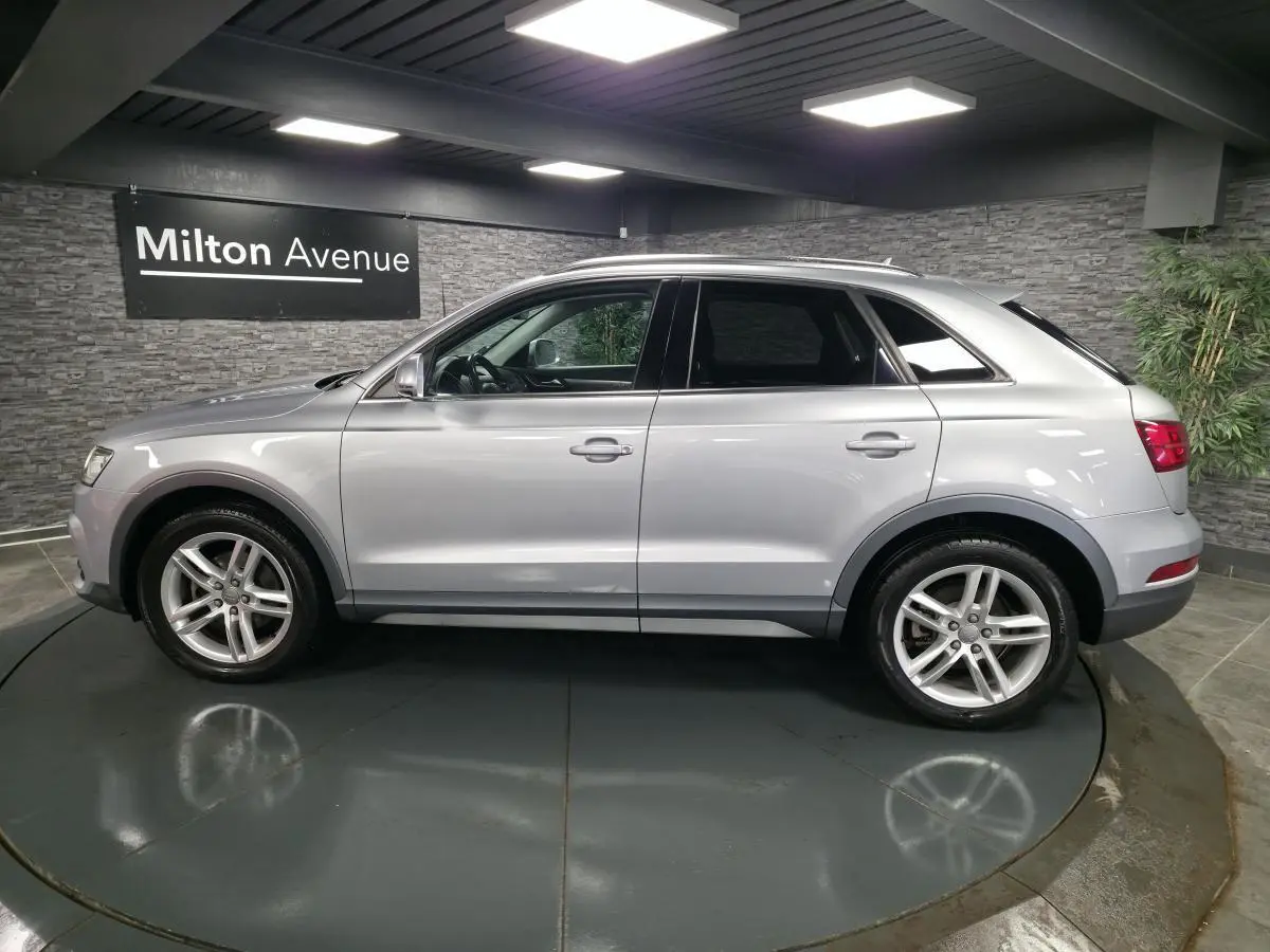 Audi Q3 gris métallisé vue de profil côté gauche dans un showroom avec jantes en alliage cinq branches.