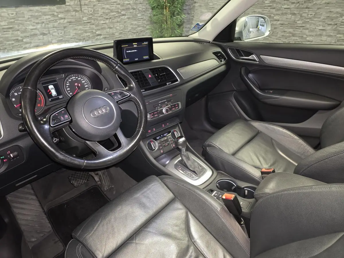 Vue intérieure côté conducteur de l'Audi Q3 2016, sellerie cuir noir et tableau de bord avec écran central.