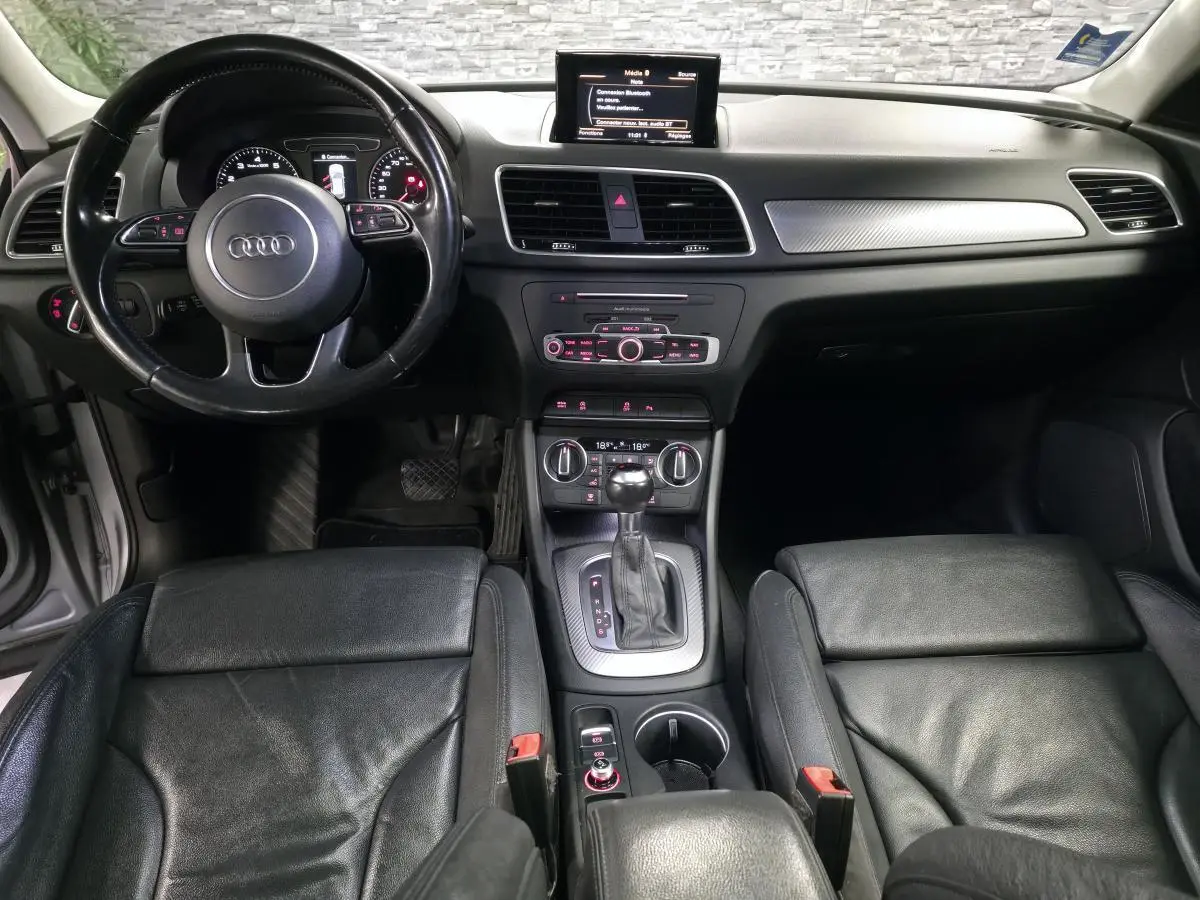 Vue intérieure avant de l'Audi Q3 1.4 TFSI 2016 avec sellerie cuir noire, console centrale et volant multifonction.