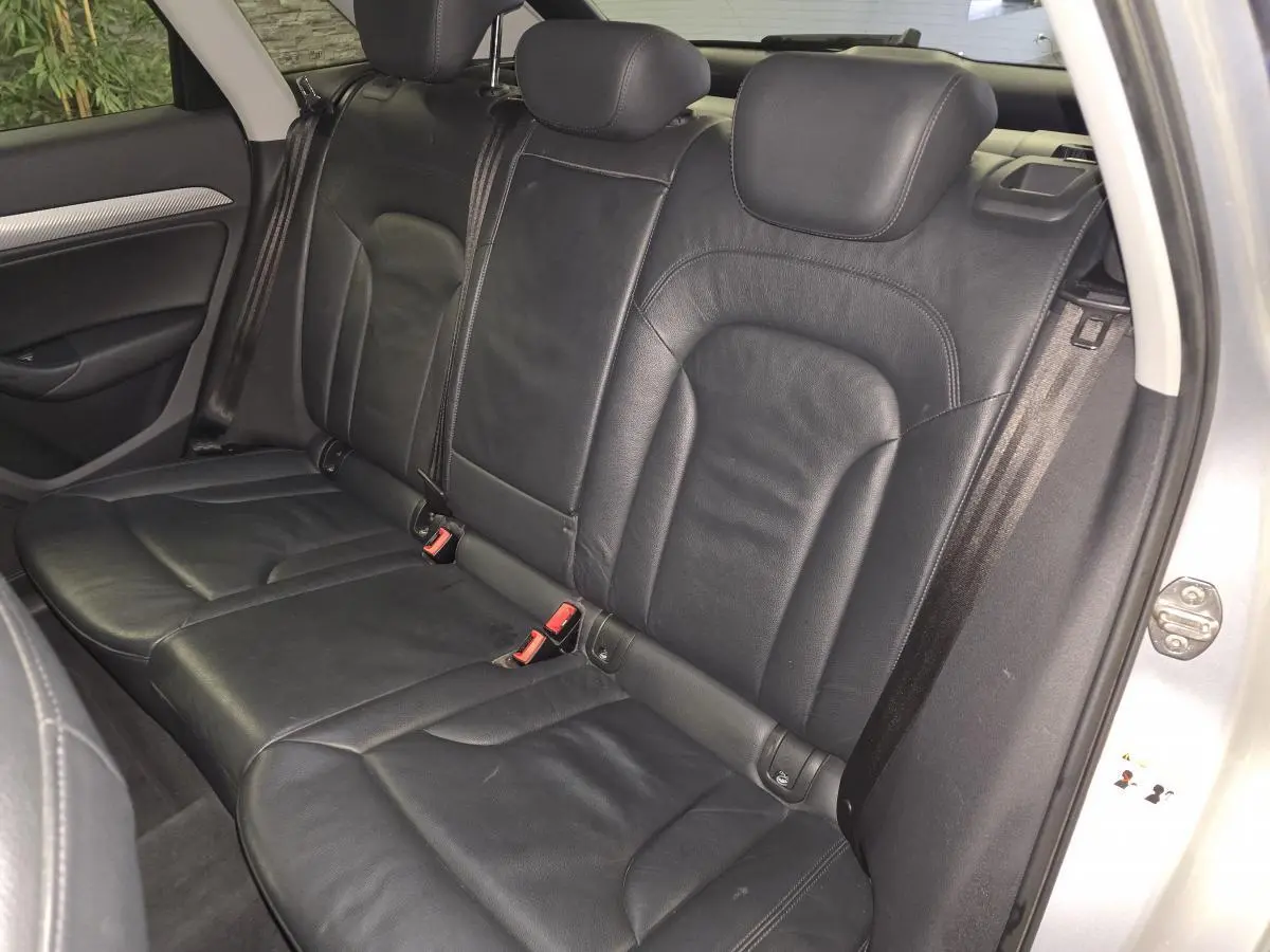 Vue intérieure côté droit sur la banquette arrière en cuir noir de l'Audi Q3 gris 2016 avec ceintures de sécurité visibles.
