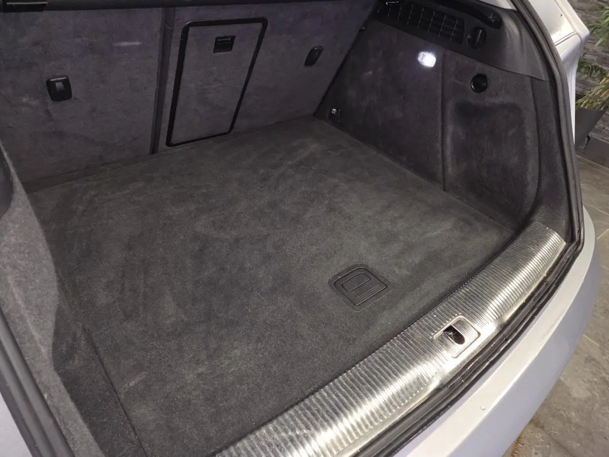 Vue du coffre ouvert de l'Audi Q3 gris, montrant la moquette noire et la garniture avec éclairage intérieur.