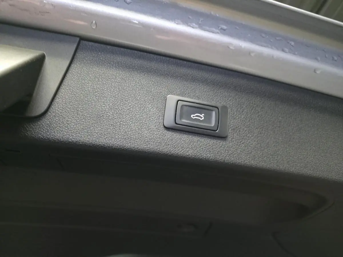 Bouton d'ouverture électrique du coffre sur la trappe intérieure d'un Audi Q3 gris, vue rapprochée.