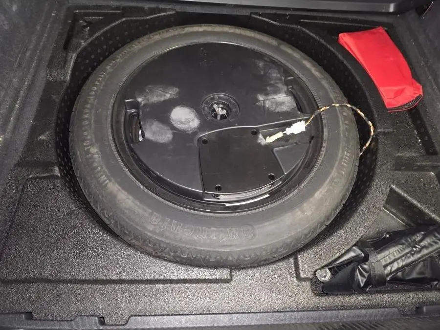 Vue rapprochée de la roue de secours noire dans le coffre d'un Audi Q3 gris, avec trousse de secours rouge à côté.