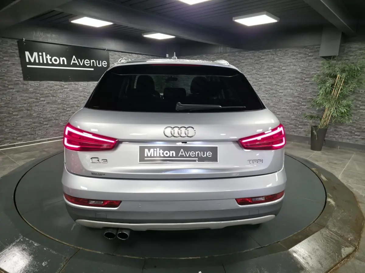 Vue arrière d'un Audi Q3 gris métallisé avec feux LED allumés et double sortie d'échappement visible.