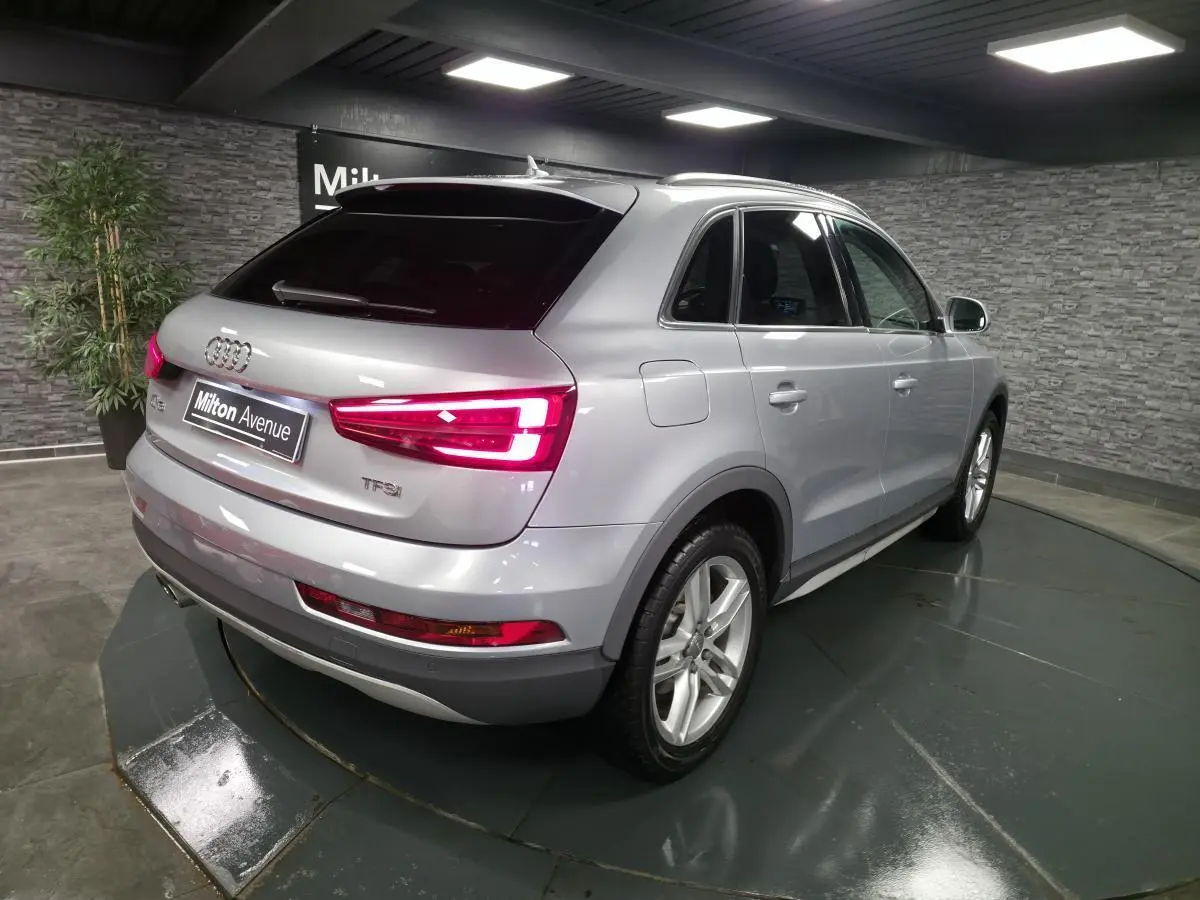 Audi Q3 gris métallisé vue 3/4 arrière droit avec feux arrière LED allumés en intérieur showroom.