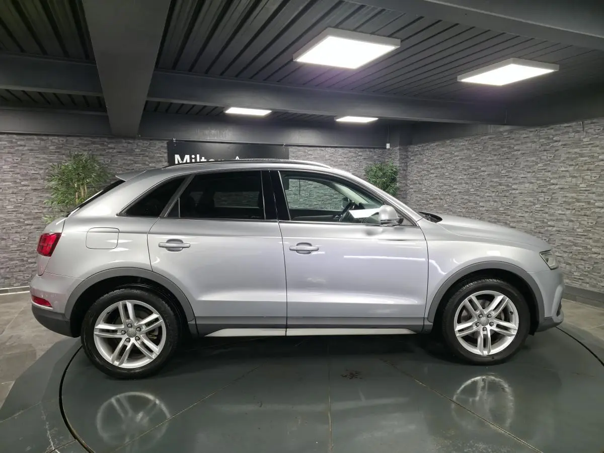 Audi Q3 gris métallisé vue de profil côté gauche dans un showroom avec jantes aluminium 5 branches doubles.