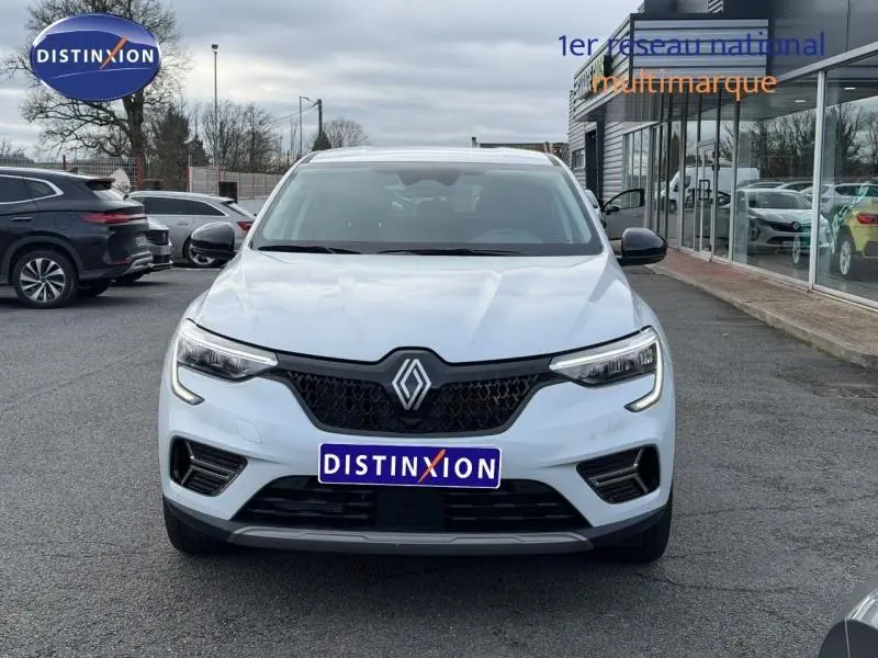 Vue frontale d'un Renault Arkana blanc 2025 avec calandre noire et logo Renault bien visible, stationné devant un showroom.