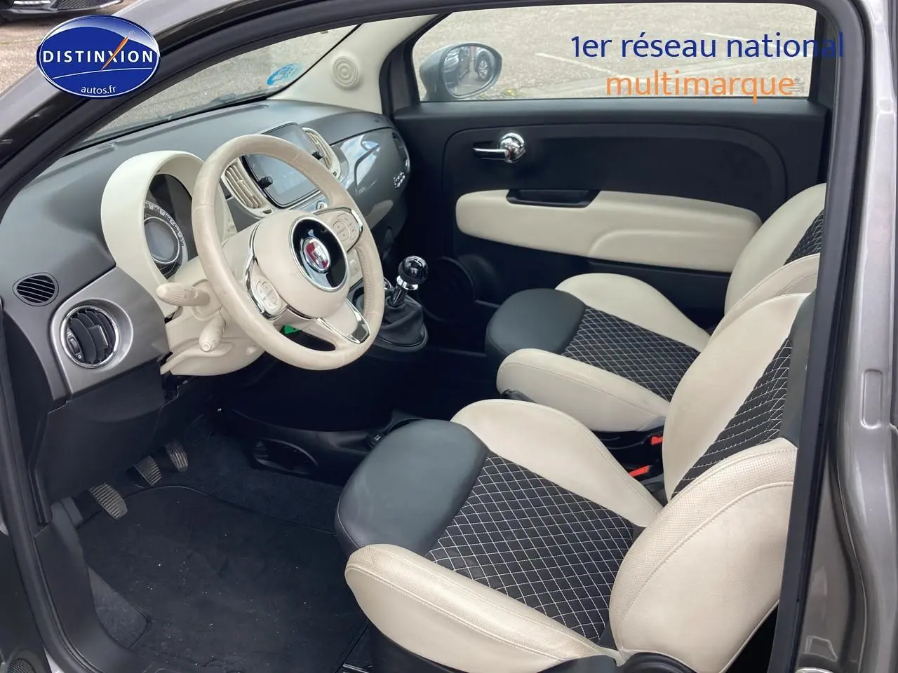 Vue intérieure côté conducteur de la Fiat 500 gris, avec volant beige, sièges bicolores et tableau de bord moderne.
