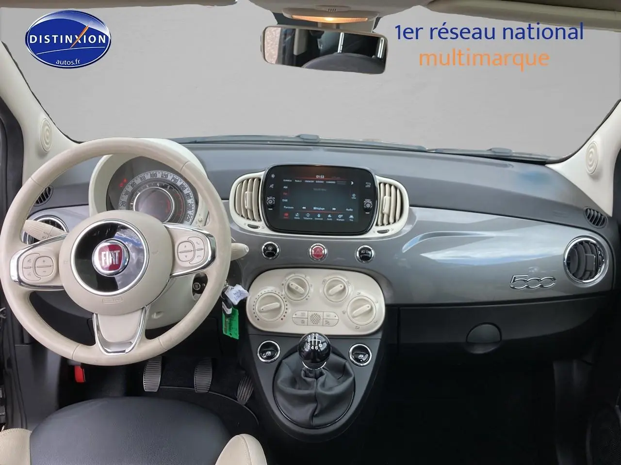 Vue intérieure frontale du tableau de bord gris et beige de la Fiat 500 1.0 70 bsg Dolcevita avec volant cuir et boîte manuelle.