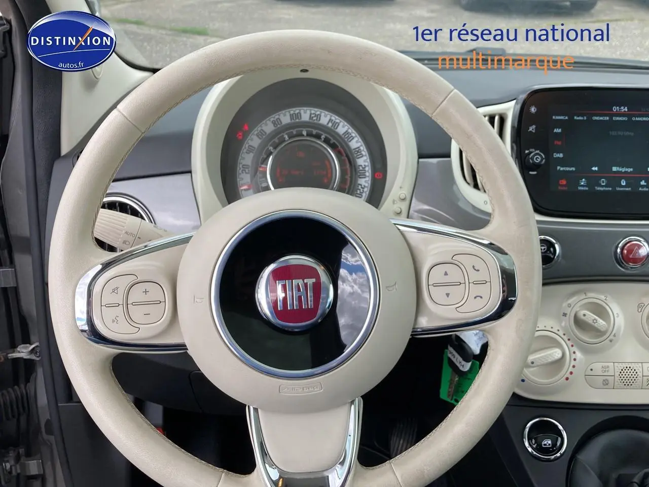 Vue intérieure centrée sur le volant beige de la Fiat 500 2022 avec tableau de bord et écran tactile visible.