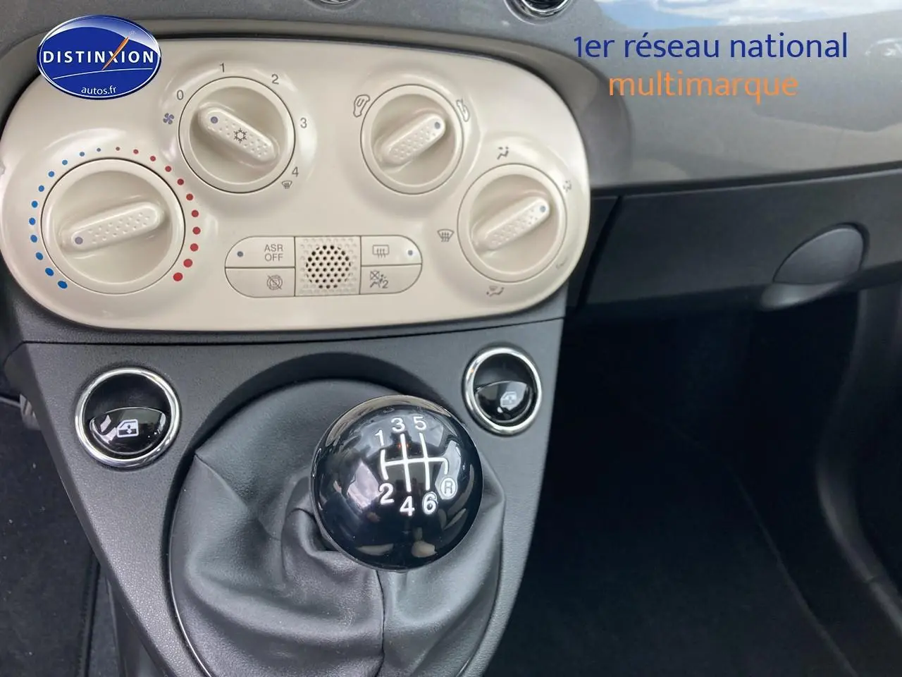 Gros plan sur la commande de boîte manuelle noire et les réglages de climatisation beige dans l’habitacle gris d’une Fiat 500.