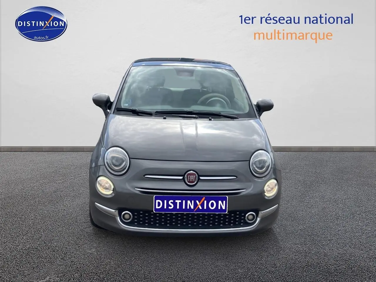 Vue frontale d'une FIAT 500 gris métallisé avec phares ronds et toit panoramique en verre visible.