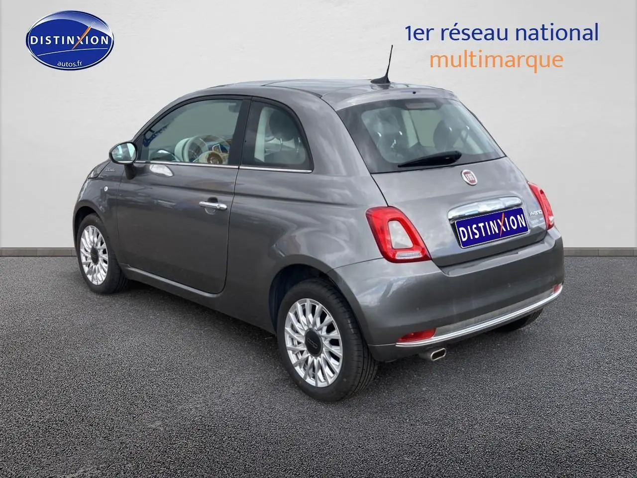 Vue 3/4 arrière droite d'une Fiat 500 gris métallisé avec jantes alu et toit panoramique en verre.