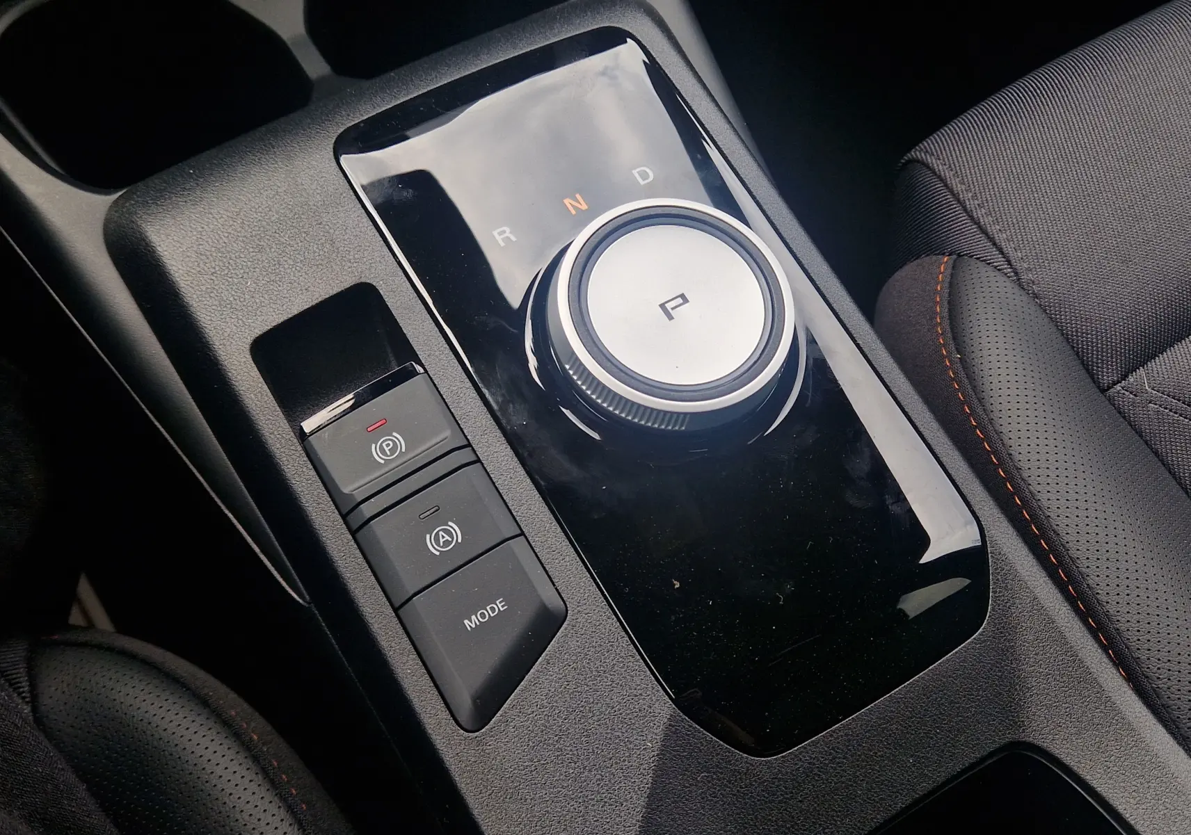 Gros plan sur la molette de boîte automatique et commandes de mode, intérieur noir avec surpiqûres orange du MG3 1.5L Hybrid+ 2026.