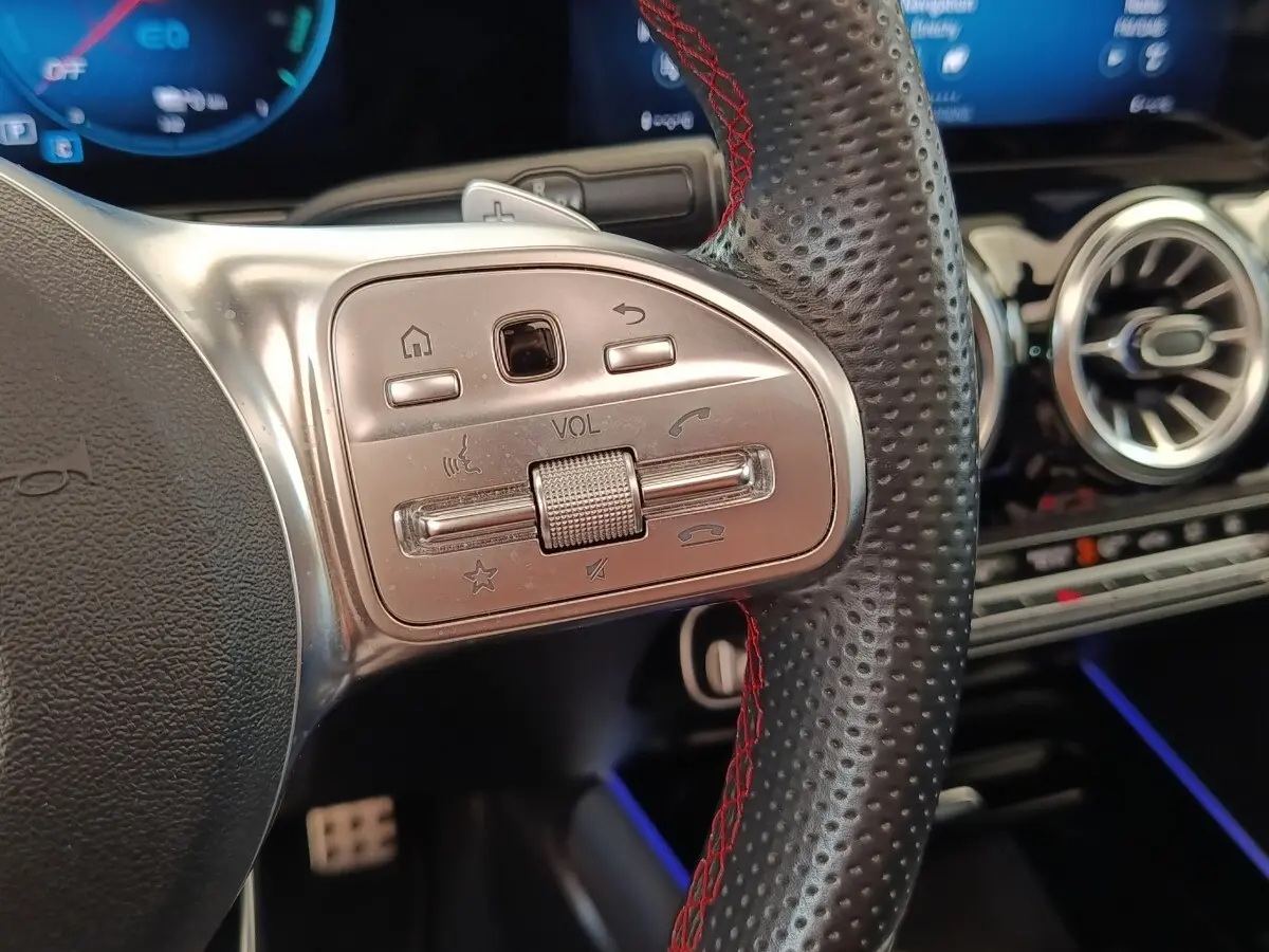 Gros plan sur le volant cuir perforé avec surpiqûres rouges du Mercedes GLA 250 e AMG Line, commandes audio intégrées.