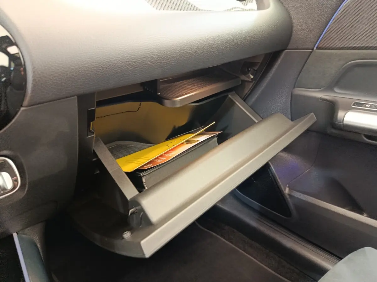 Gros plan sur la boîte à gants ouverte côté passager du Mercedes GLA 250 e AMG Line noir, intérieur sombre.