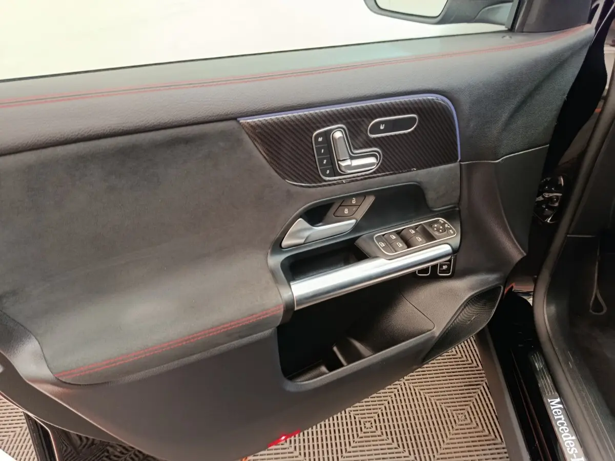 Vue intérieure côté conducteur de la porte noire du Mercedes GLA 250 e AMG Line avec surpiqûres rouges et commandes intégrées.