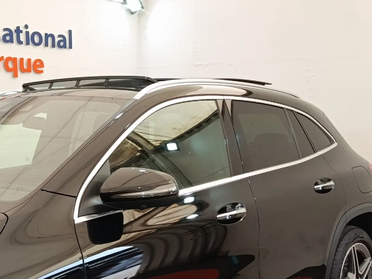Vue latérale côté gauche d’un Mercedes GLA 250 e AMG Line noir brillant avec rails de toit chromés.