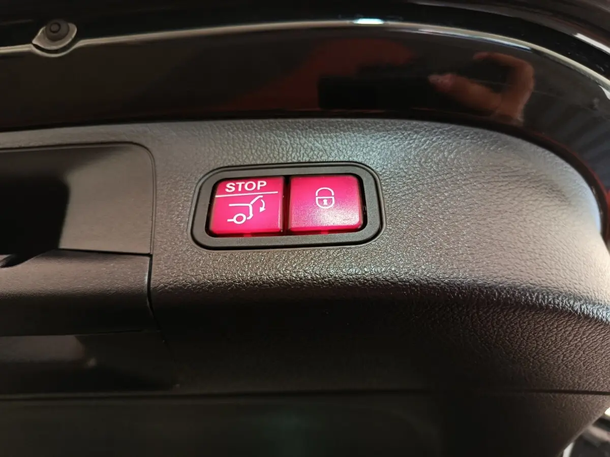Boutons rouges d'ouverture et fermeture électrique du coffre sur la garniture intérieure noire d'un Mercedes GLA 250 e AMG Line.