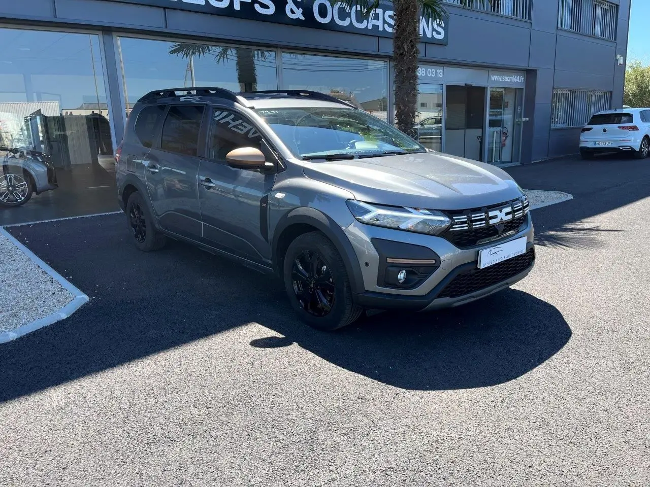 Dacia Jogger gris schiste en 3/4 avant droit, avec jantes noires et détails noirs sur la calandre et les bas de caisse.