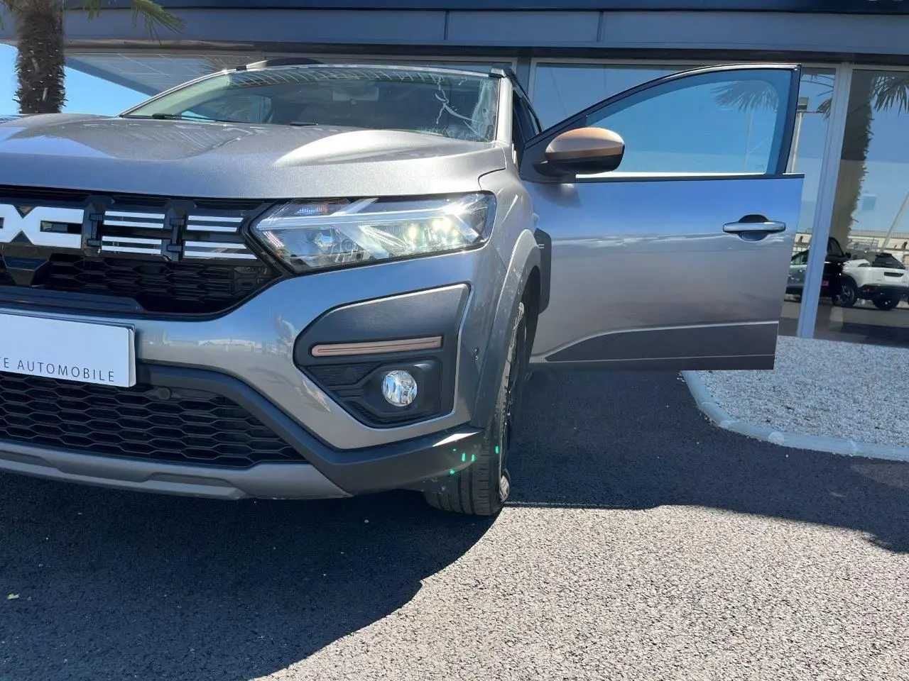 Vue avant droite du Dacia Jogger gris schiste 2025 avec porte ouverte et phares allumés, version hybride 7 places.