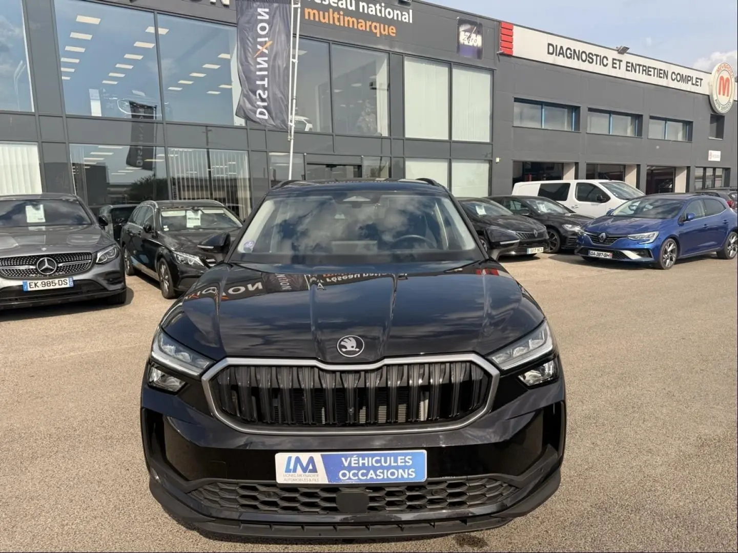 Vue avant d'un Skoda Kodiaq noir 2024 avec calandre verticale distinctive, stationné devant un garage multimarque.