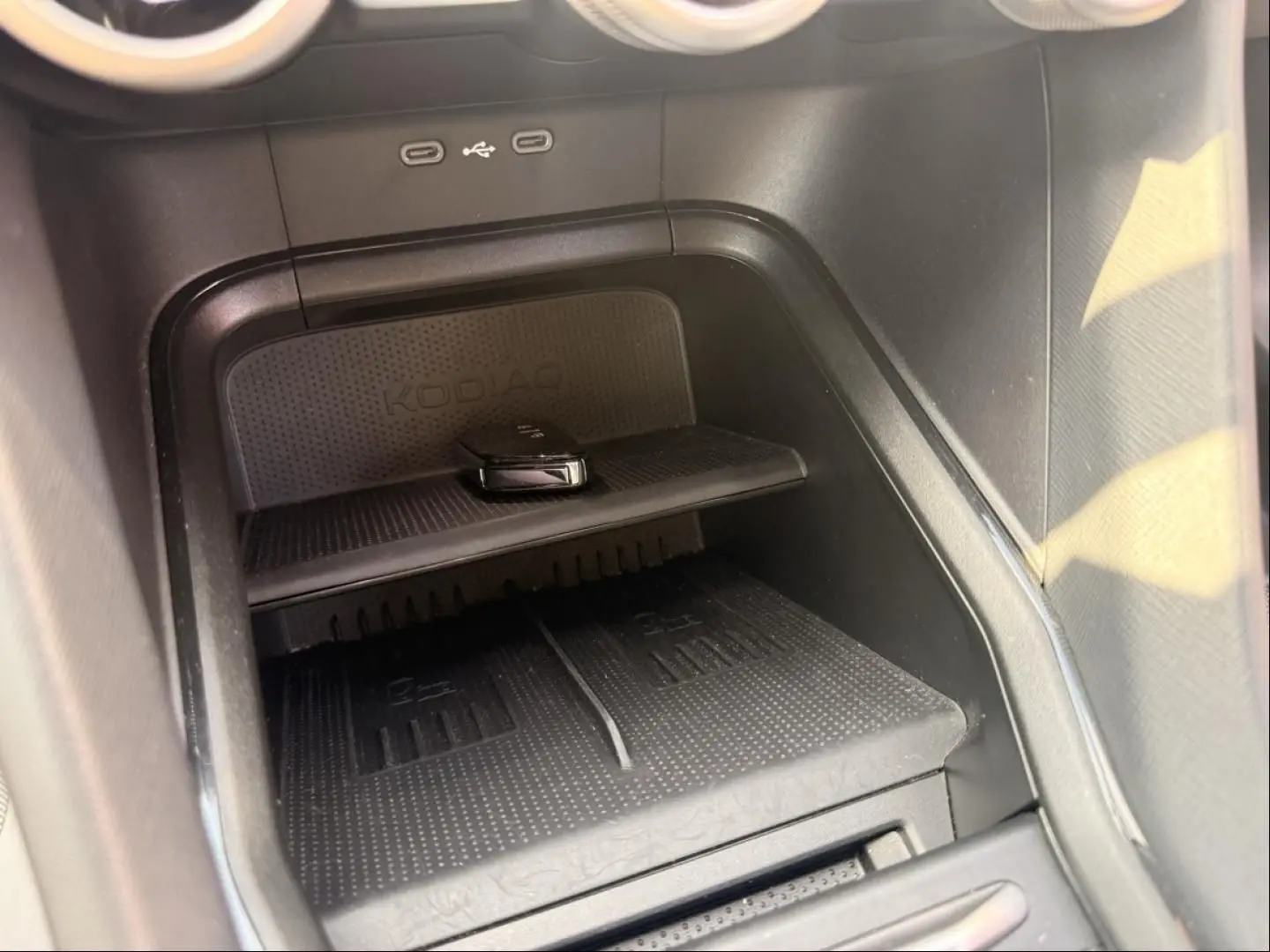 Détail de la console centrale noire du Skoda Kodiaq 2024 montrant un espace de rangement avec chargeur sans fil et ports USB.