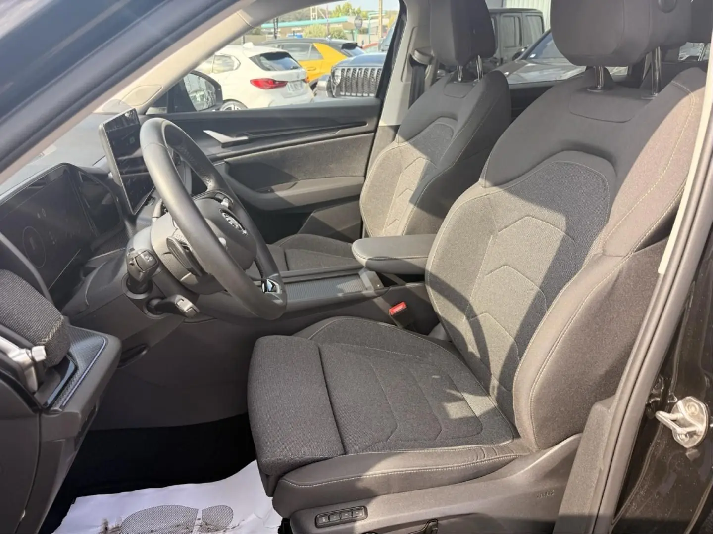 Intérieur avant droit du Skoda Kodiaq 2024 noir, sièges tissu gris et tableau de bord avec écran tactile.