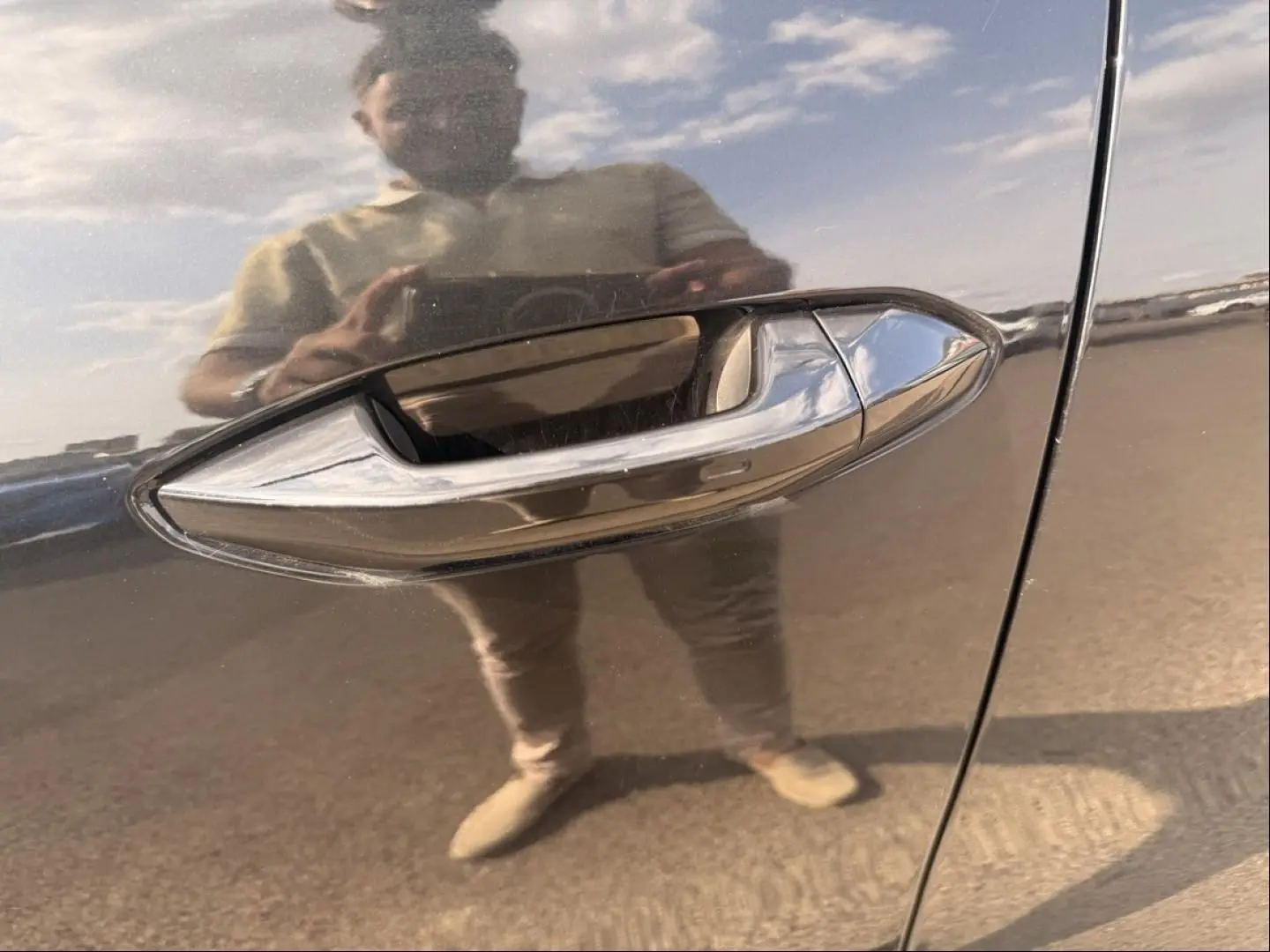 Poignée de porte chromée en gros plan sur une Skoda Kodiaq noire 2024, reflet d'une personne visible sur la carrosserie.