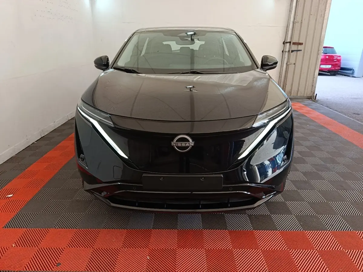 Vue de face d'une Nissan Ariya noire 2026 avec phares LED fins et calandre lisse dans un garage.