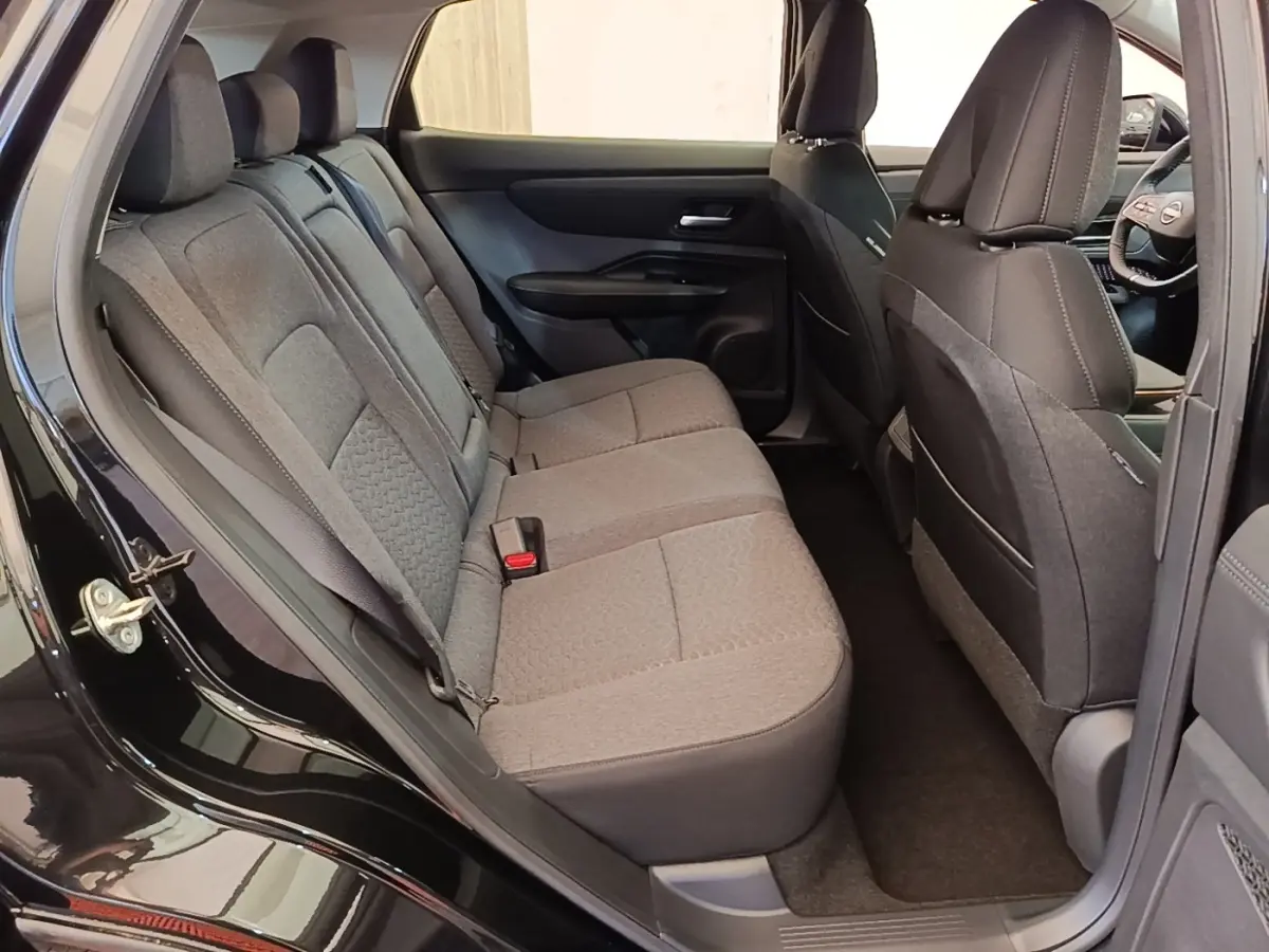Vue intérieure côté gauche montrant la banquette arrière grise du Nissan Ariya noir 2026 avec sièges tissu et ceintures visibles.