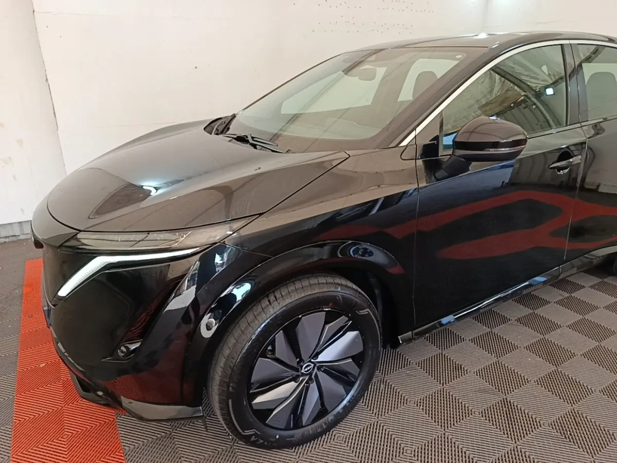 Vue 3/4 avant droit du Nissan Ariya noir avec phares LED et jantes au design moderne, stationné en intérieur.