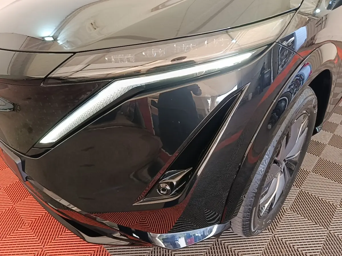 Gros plan sur l'avant droit noir brillant du Nissan Ariya 63kWh avec phares LED et jante moderne visible.
