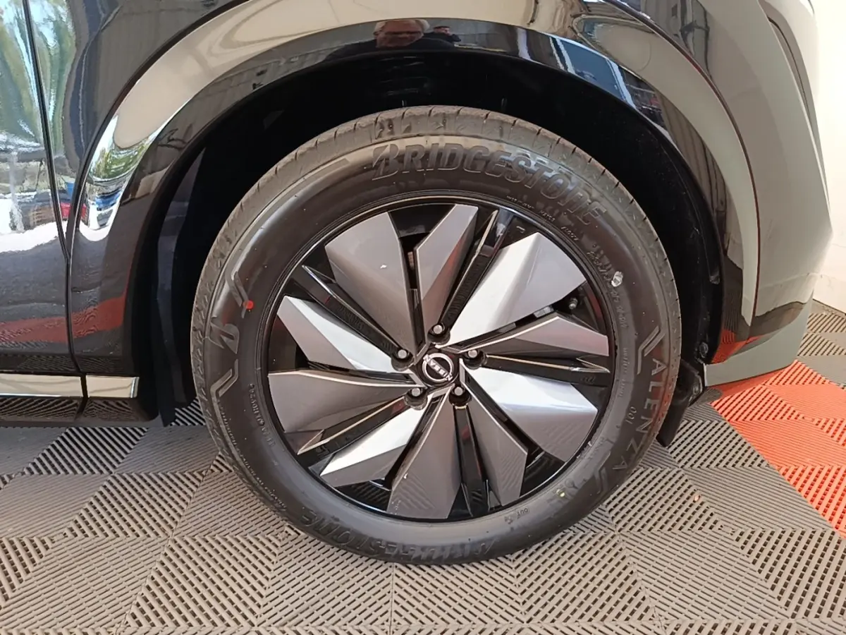 Gros plan sur la roue avant droite du Nissan Ariya noir, mettant en valeur la jante design bicolore et le pneu Bridgestone.