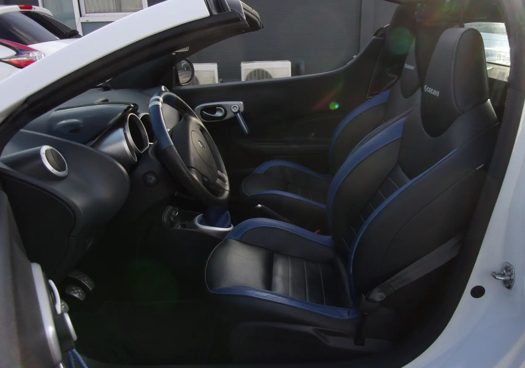 Intérieur côté gauche d'une Renault Wind blanc glacier 2012, sièges sport cuir noir et bleu avec logo Gordini.