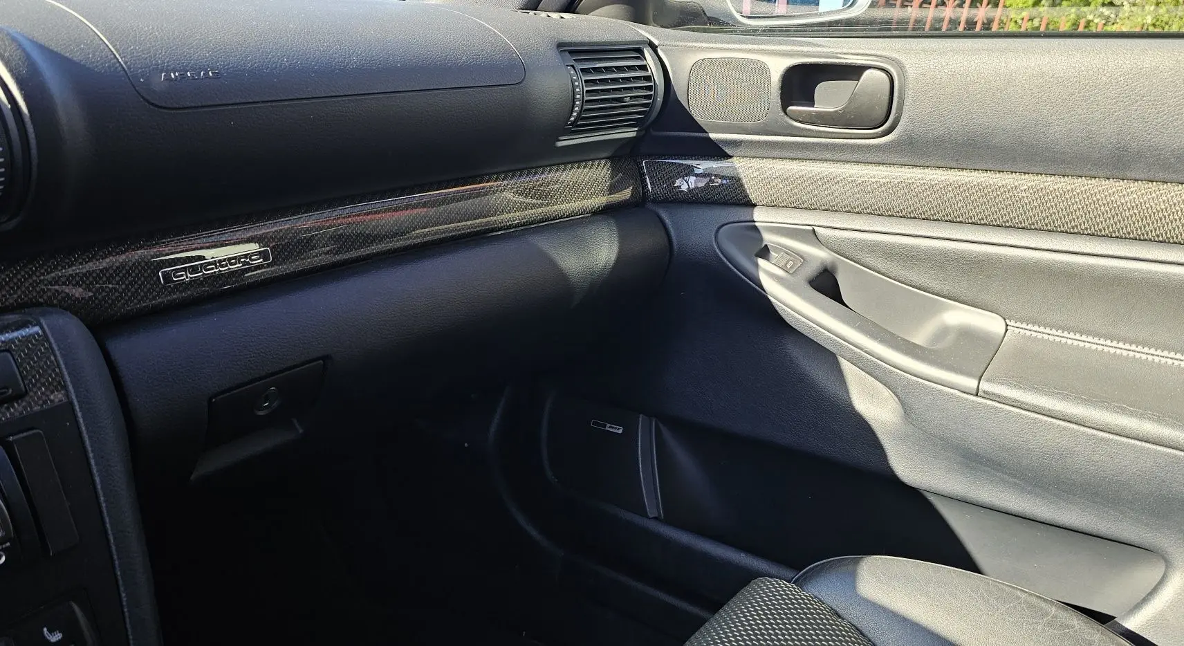 Intérieur côté passager de l'Audi RS4 Avant B5 2001, tableau de bord et porte en cuir noir avec insert carbone Quattro.