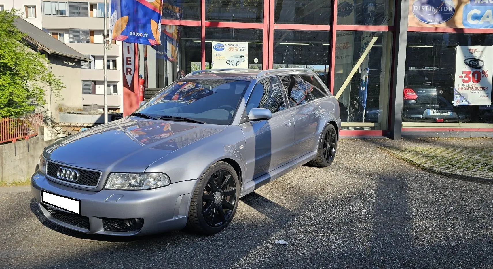 Audi RS4 Avant gris vue 3/4 avant droit, avec jantes noires et carrosserie brillante sous le soleil.