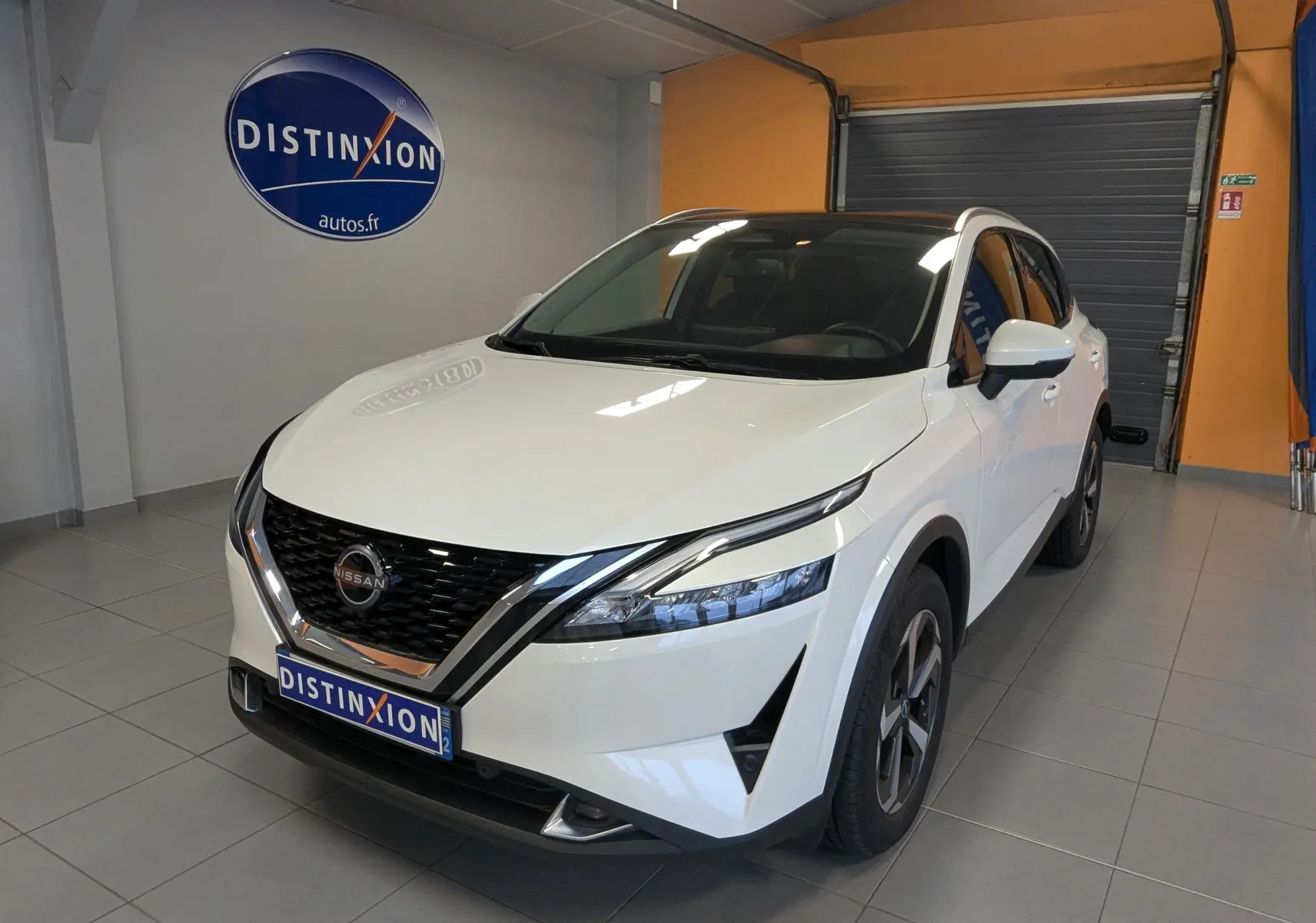 Nissan Qashqai 2024 blanc vu en 3/4 avant droit, avec calandre noire et jantes bi-ton visibles en intérieur showroom.