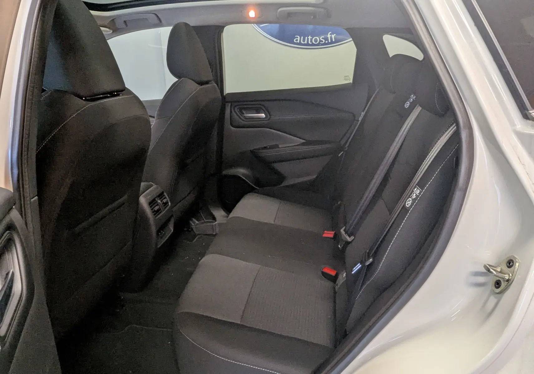 Vue intérieure côté droit sur la banquette arrière noire du Nissan Qashqai blanc 2024 avec porte ouverte.