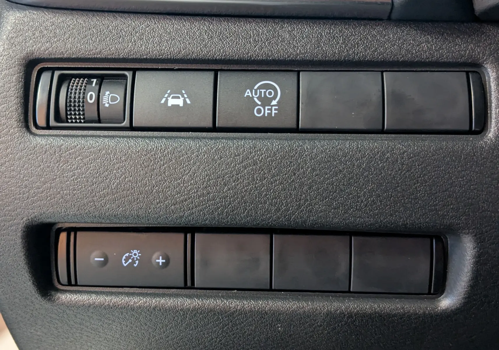 Gros plan sur les commandes noires du tableau de bord du Nissan Qashqai blanc 2024, avec réglage phares et assistance conduite.