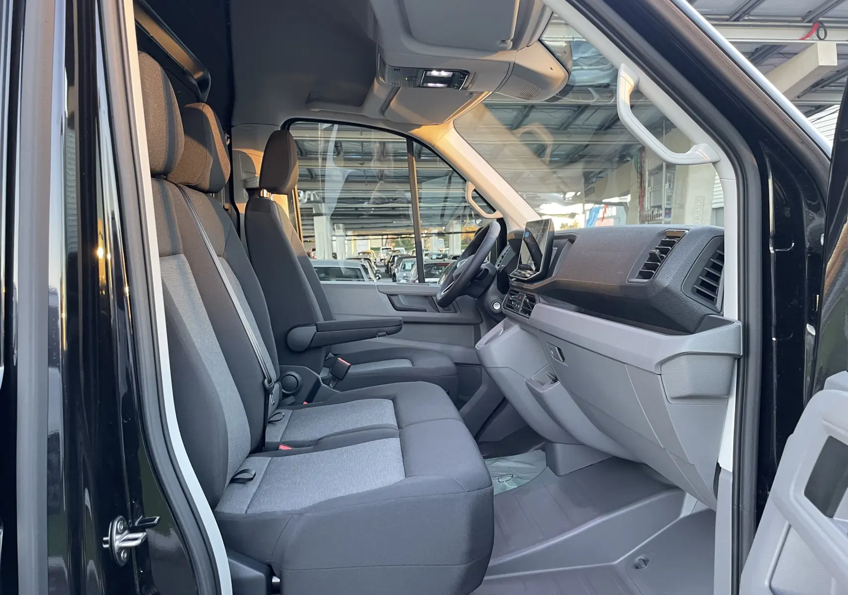 Vue intérieure côté gauche du Volkswagen Crafter Van 2025 noir intense, montrant les sièges avant et le tableau de bord moderne.