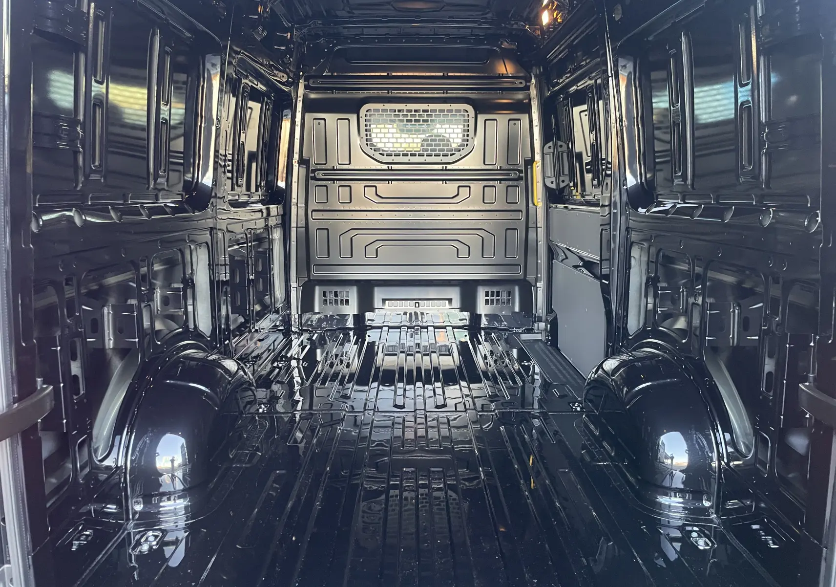 Vue intérieure arrière du Volkswagen Crafter Van noir intense, montrant l'espace de chargement vide et la cloison avec vitre fixe.