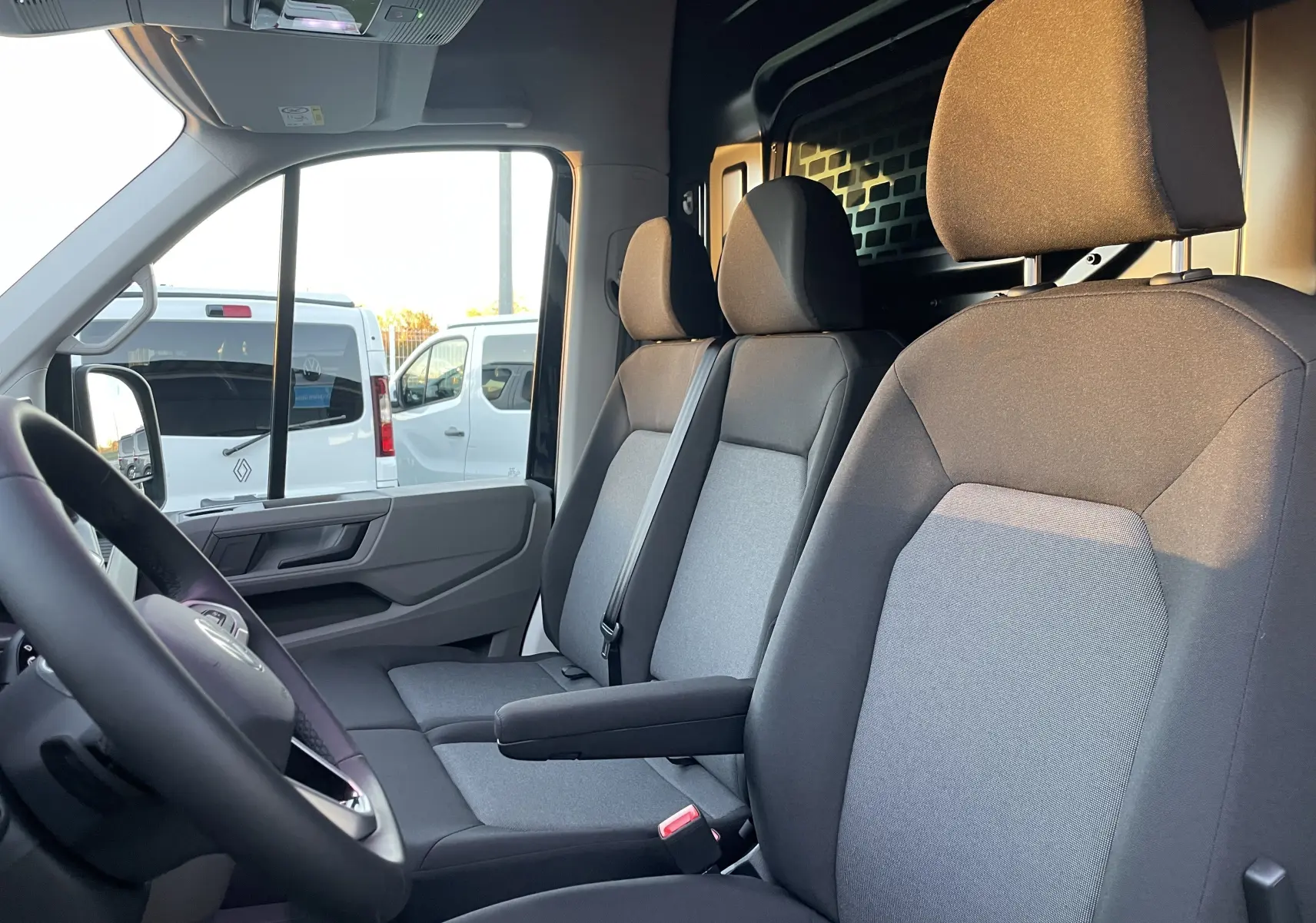 Vue intérieure côté conducteur du Volkswagen Crafter Van 2025, sièges tissu gris et cloison avec vitre fixe noire.
