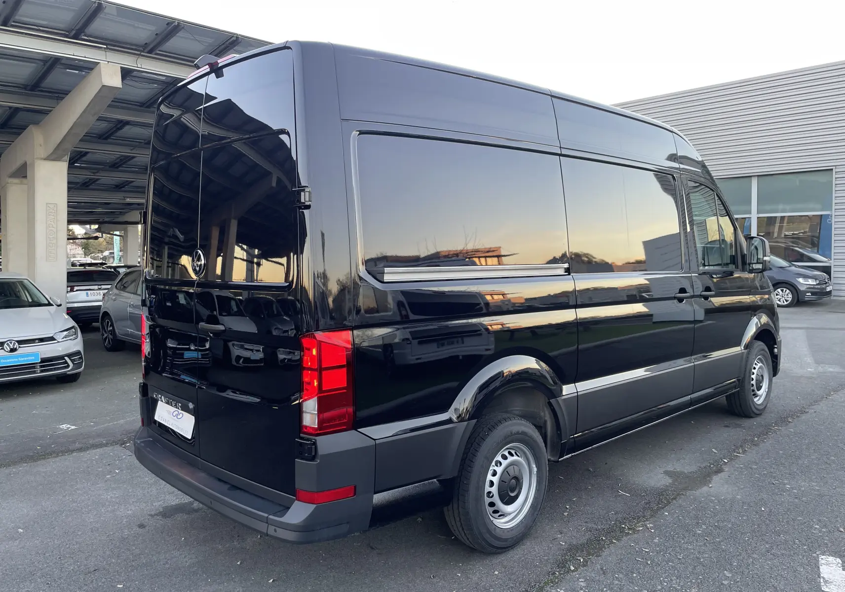 Vue 3/4 arrière droite d'un Volkswagen Crafter Van noir intense garé, avec vitres teintées et feux arrière rouges visibles.