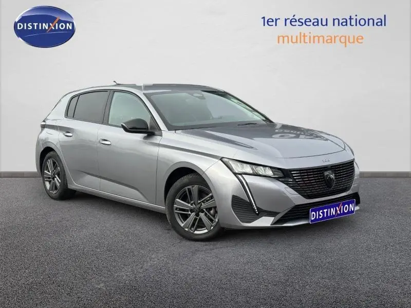 Peugeot 308 gris Artense vue 3/4 avant droit, avec calandre noire distinctive et jantes alliage foncé.