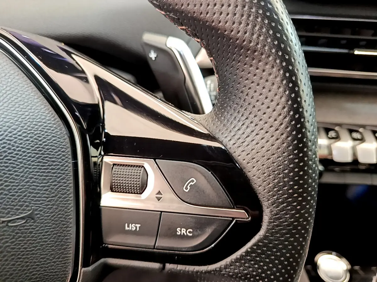 Gros plan sur le volant cuir perforé côté gauche du Peugeot 3008 rouge, avec commandes audio et téléphone intégrées.