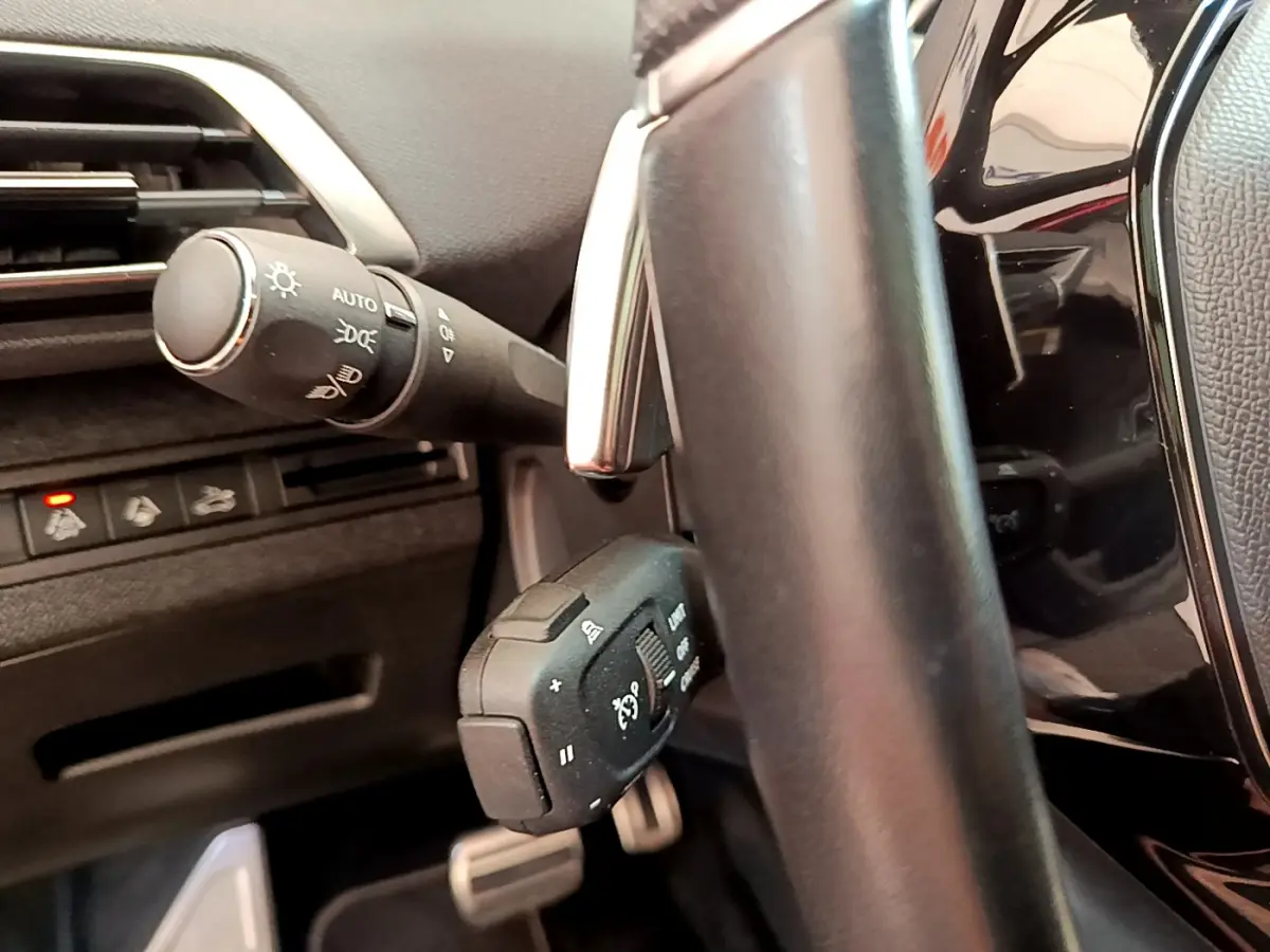 Gros plan sur la commande des phares et régulateur de vitesse derrière le volant cuir d’un Peugeot 3008 rouge.