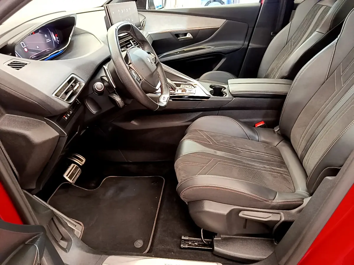 Vue intérieure côté conducteur du Peugeot 3008 rouge 2021, avec volant cuir et sièges en tissu noir.