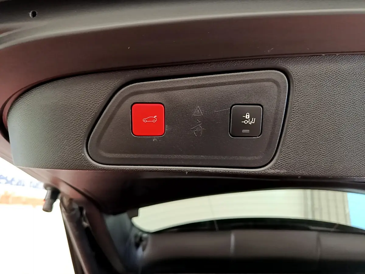 Gros plan sur les boutons d'ouverture et de verrouillage du hayon intérieur d'un Peugeot 3008 rouge, vue depuis l'arrière ouverte.