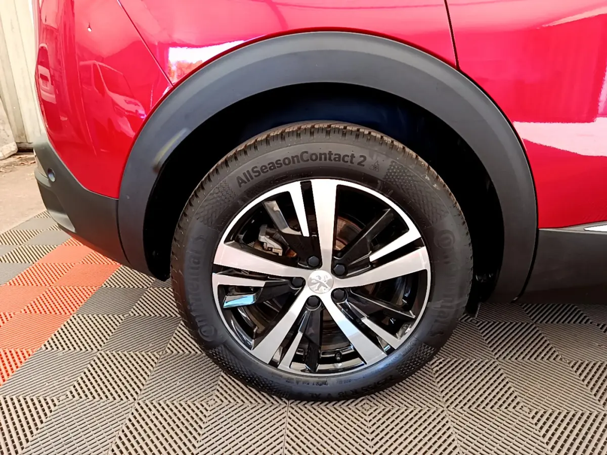 Gros plan sur la roue arrière droite du Peugeot 3008 rouge, avec jante alliage bicolore et pneu toutes saisons.